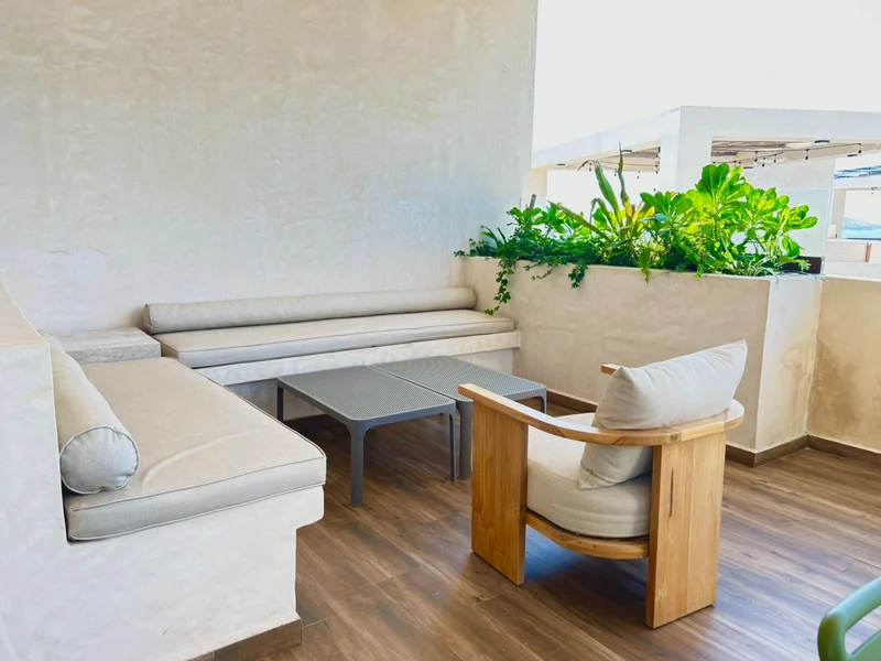 Lounge de azotea Lounge de azotea en Aldea Ananta, con banca corrida de obra y cojines claros, mesas bajas, jardinera con vegetación y una pérgola con serie de foquitos.