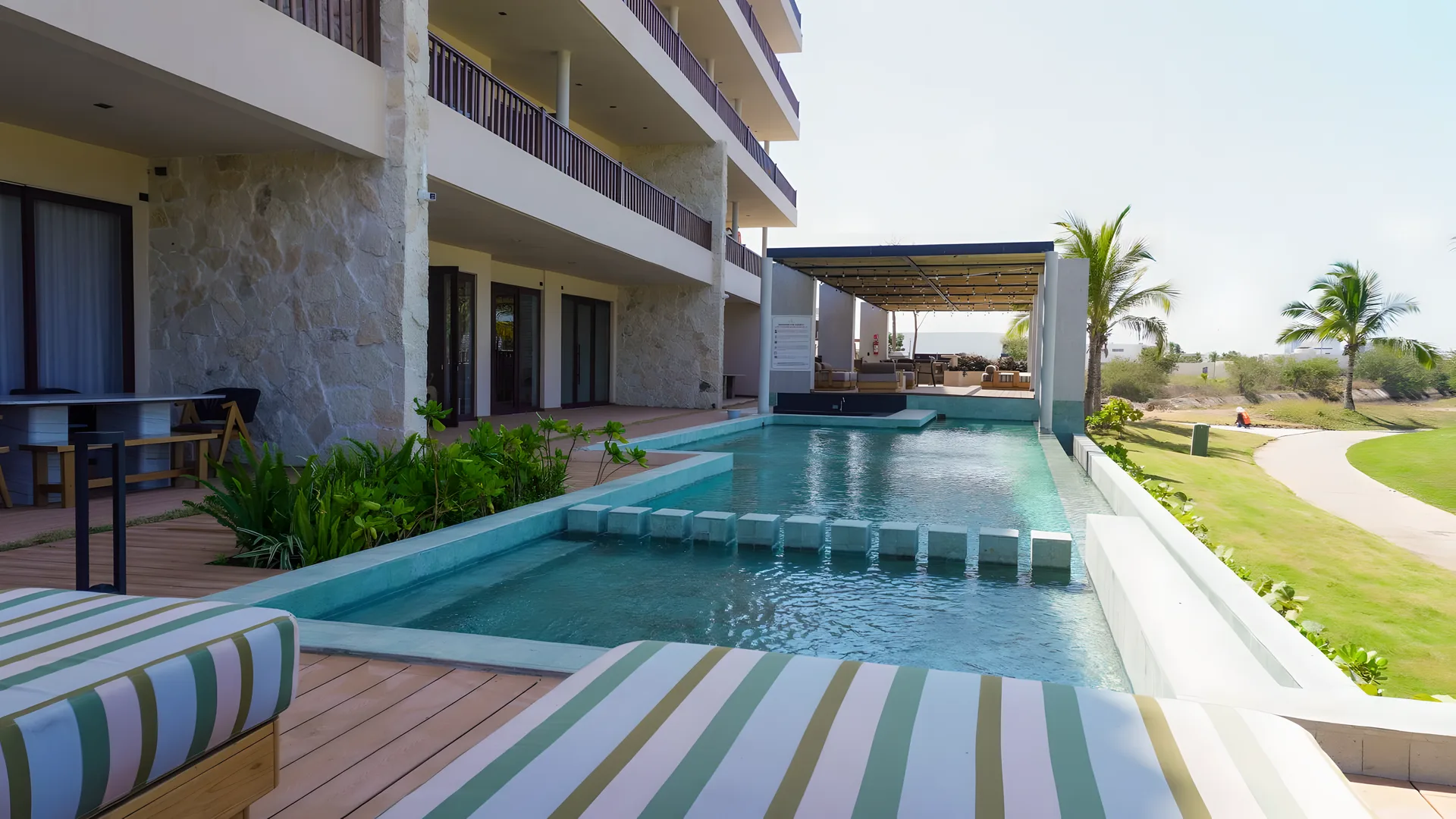 Alberca de Mangata con camastros y deck de madera, junto a la fachada de piedra del edificio en Marina Mazatlán