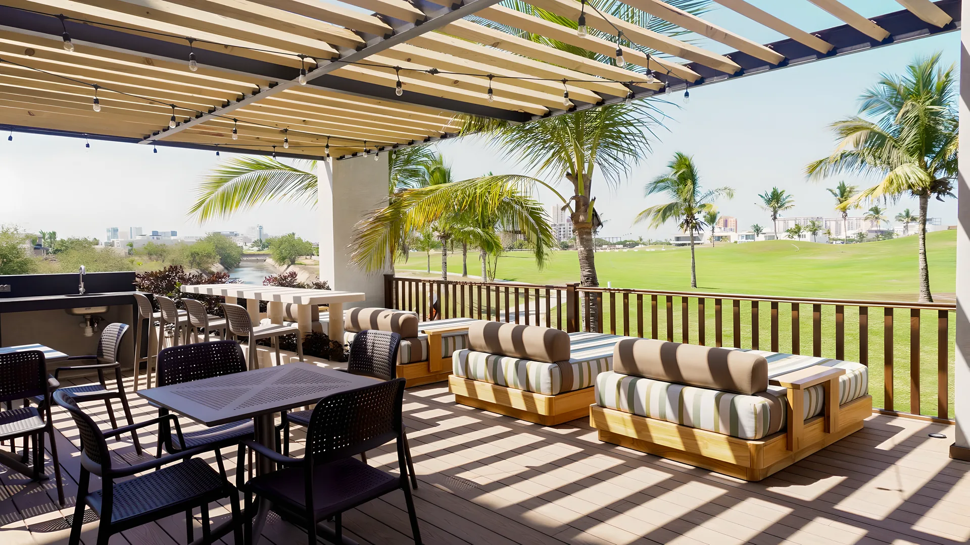 Terraza social de Mangata bajo pérgola de madera con luces colgantes, frente al campo de golf de Marina Mazatlán
